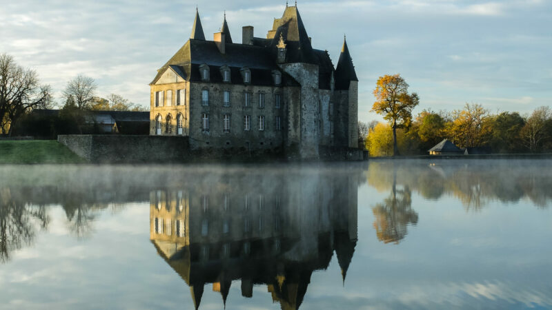 A clear lake with the reflection of a huge castle against the cloudy sky in autumn